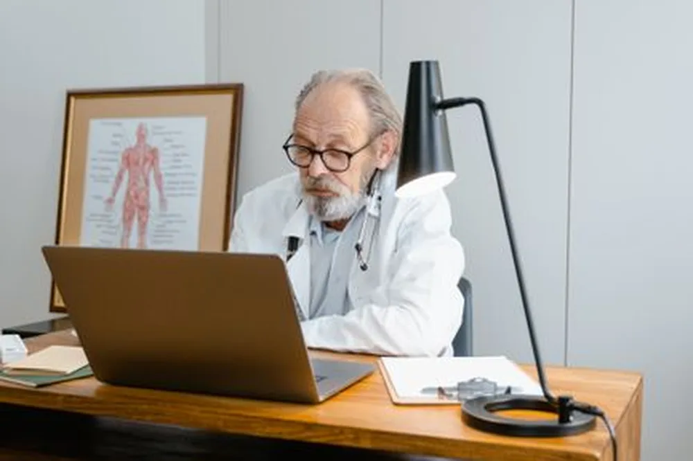 Médecin âgé utilisant un ordinateur portable pour des services de télémédecine dans un bureau.