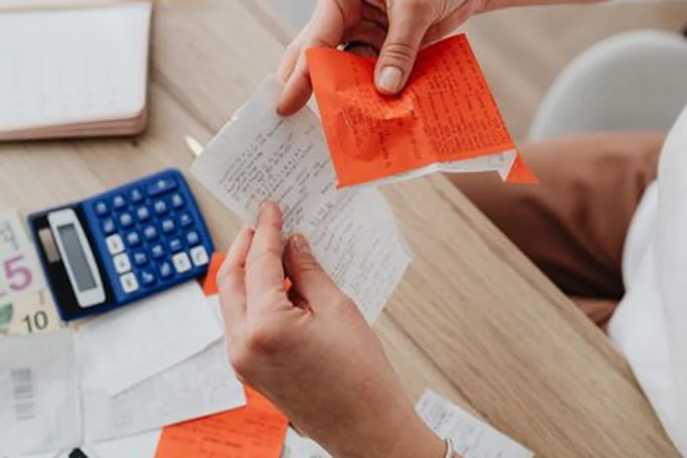 Vue de dessus d'une personne organisant ses finances avec une calculatrice, des reçus et des notes sur un bureau.