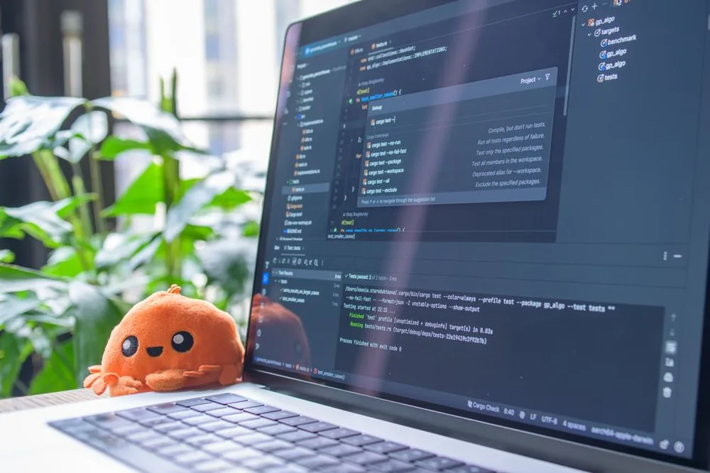 Ordinateur portable ouvert avec éditeur de code affiché, à côté d'un jouet en peluche orange et de plantes vertes.