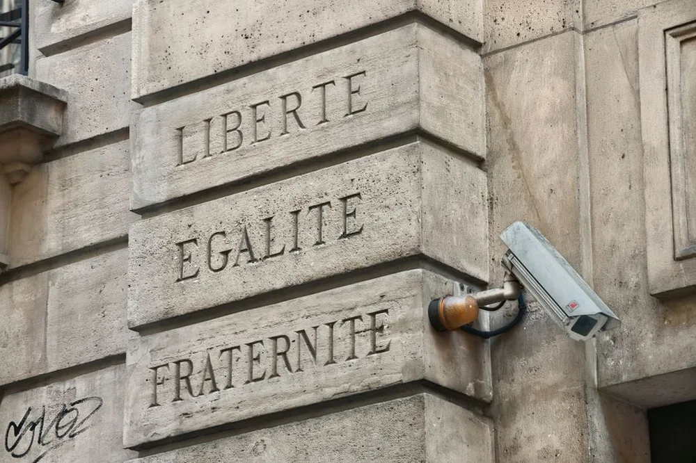 Un mur parisien avec 'Liberté, Égalité, Fraternité' et une caméra de sécurité.