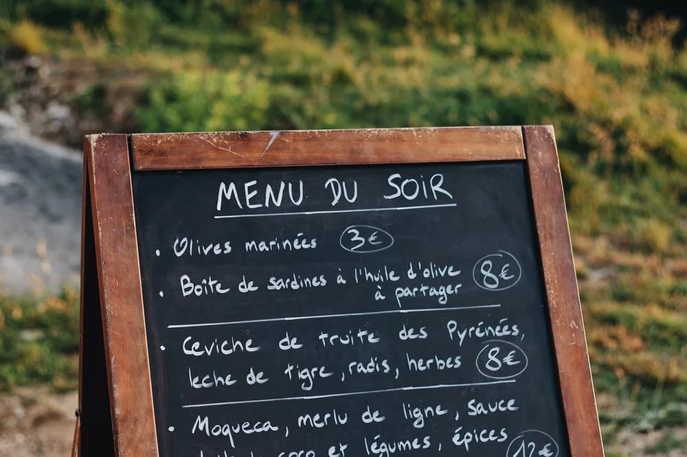 Panneau de menu en ardoise listant des plats français et leurs prix dans un cadre extérieur.