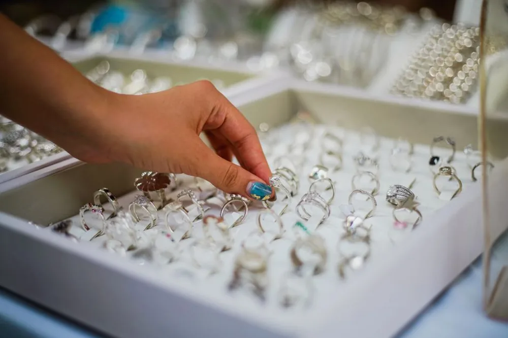 La main d'une femme choisissant délicatement une bague parmi une vitrine de bijoux élégants.
