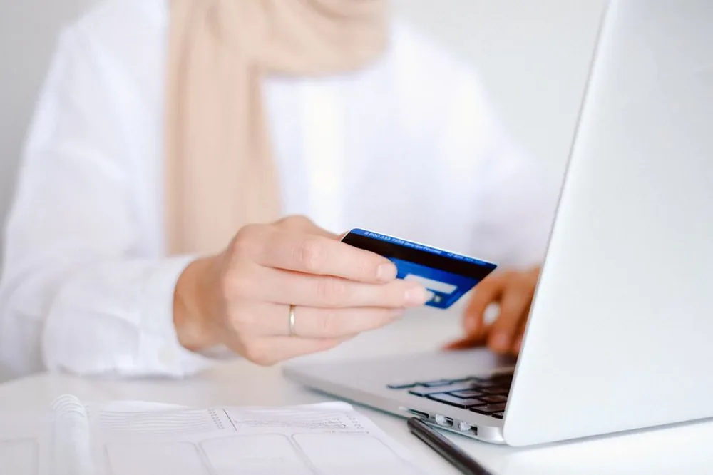 Gros plan sur une personne tenant une carte de crédit tout en utilisant un ordinateur portable pour faire des achats en ligne.