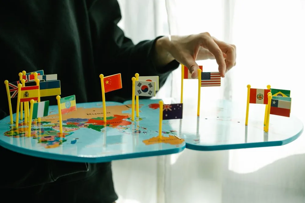 Main arrangeant des drapeaux sur une carte du monde, signifiant la diversité mondiale.