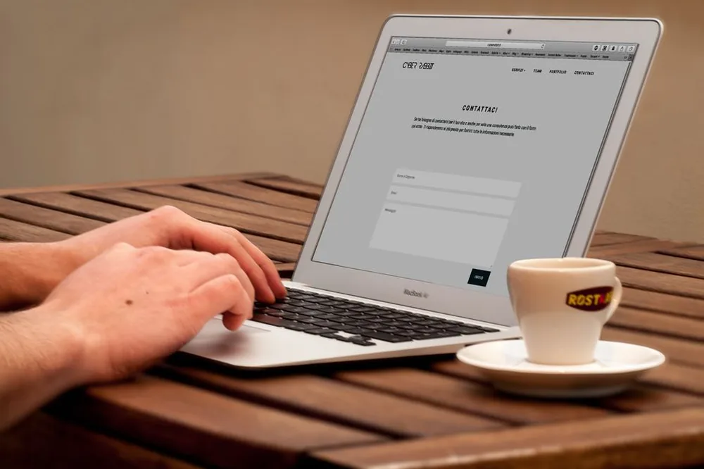 Gros plan sur des mains tapant sur un ordinateur portable à côté d'une tasse de café sur un bureau en bois.