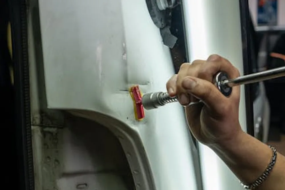 Gros plan sur la réparation d'une bosse sur un véhicule dans un garage, à l'aide d'outils spécialisés et sous un éclairage intense.