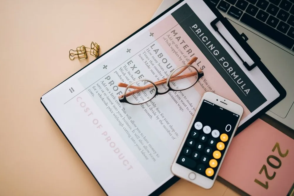 Vue aérienne d'outils professionnels comprenant une calculatrice téléphonique, un document de formule de prix et des lunettes sur un bureau.