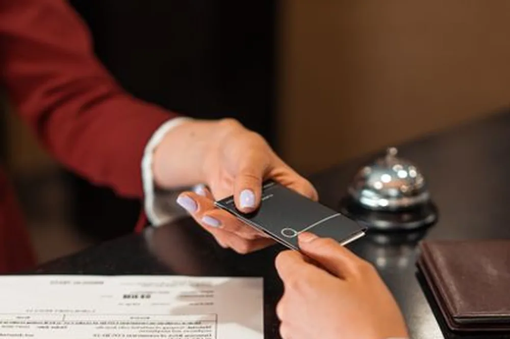 Un réceptionniste d'hôtel remet une carte de clé à un client par-dessus le comptoir, avec des documents visibles.